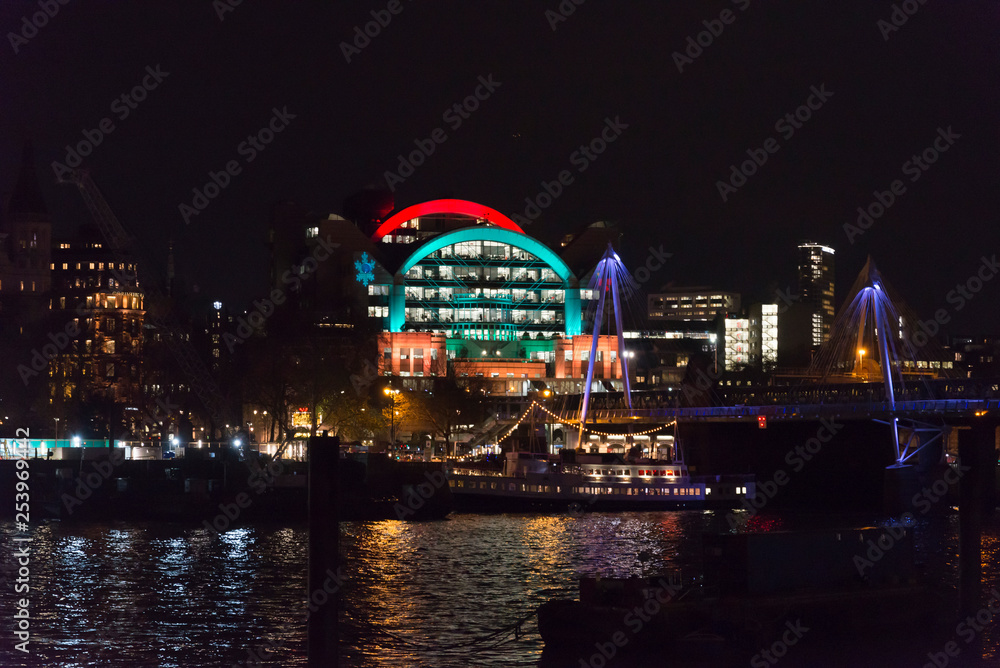 Illuminated Charing Cross railway station building in Christmas colours and Hungerford bridge at night, London, England, UK