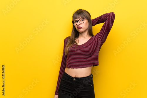 Woman with glasses over yellow wall having doubts