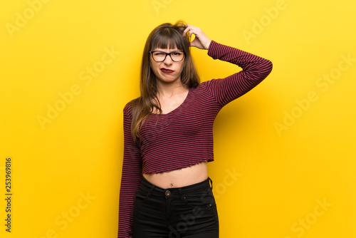 Woman with glasses over yellow wall having doubts and thinking