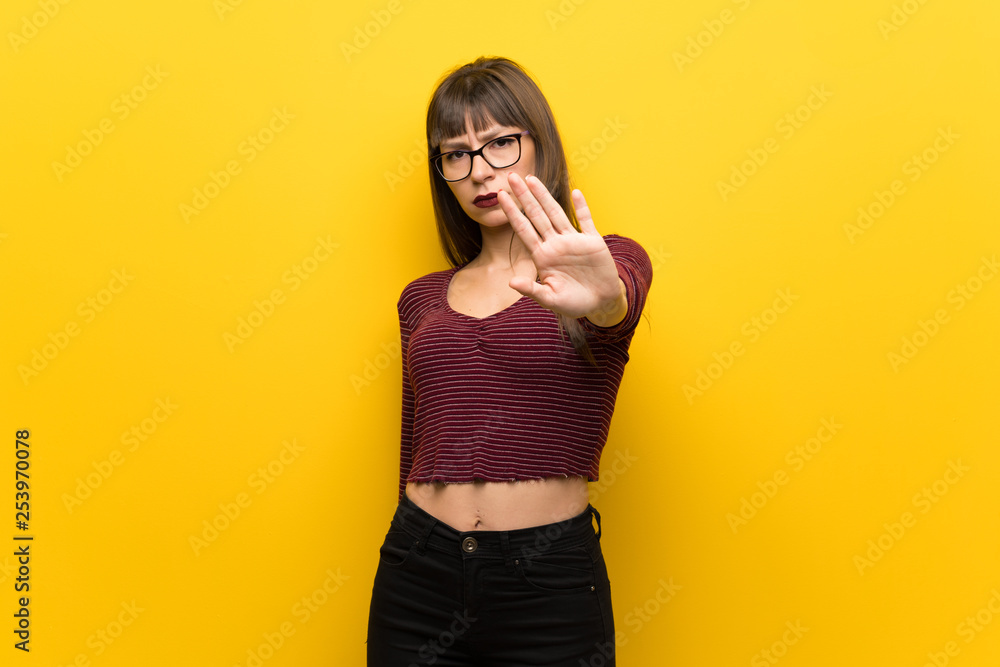 Woman with glasses over yellow wall making stop gesture denying a situation that thinks wrong Woman with glasses over yellow wall making stop gesture denying a situation that thinks wrong