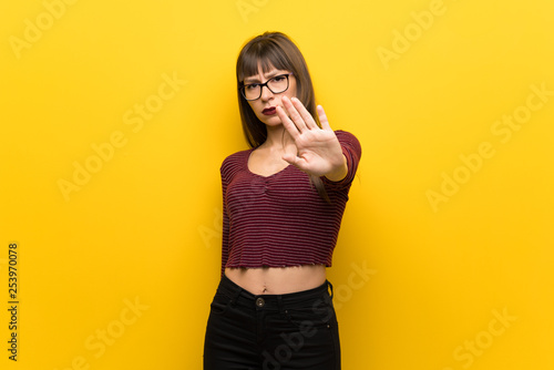 Woman with glasses over yellow wall making stop gesture denying a situation that thinks wrong
