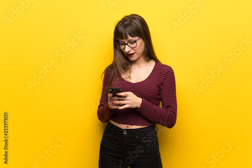 Woman with glasses over yellow wall sending a message with the mobile