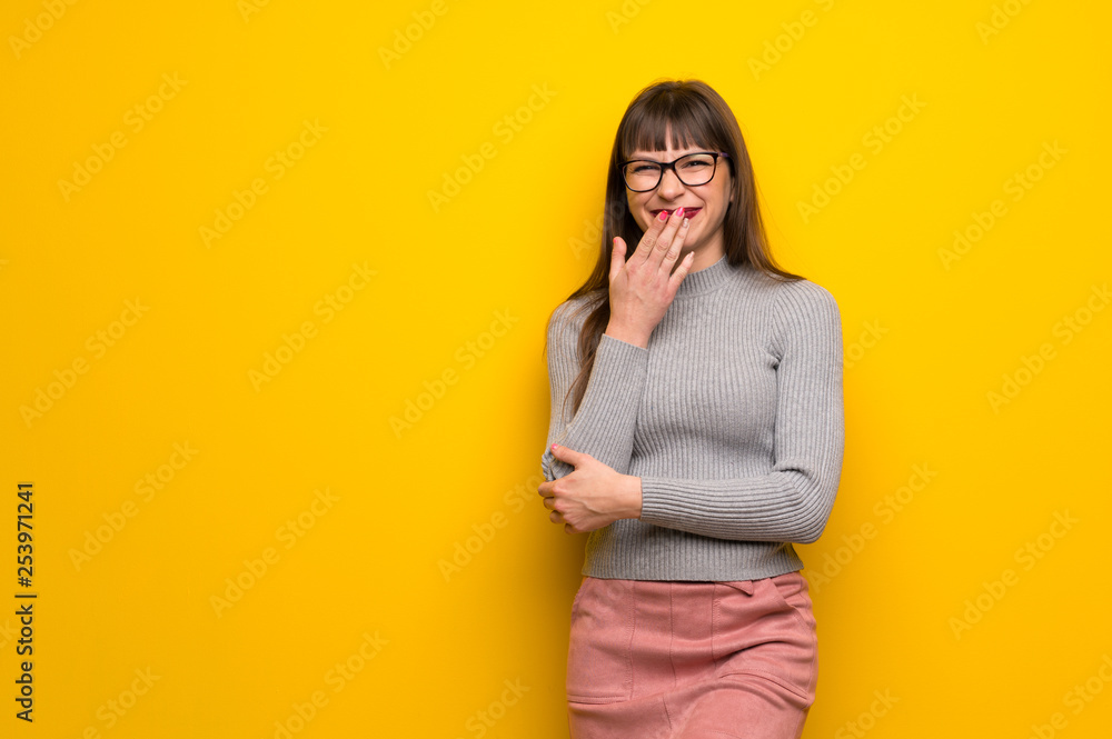 Woman with glasses over yellow wall smiling a lot while covering mouth Woman with glasses over yellow wall smiling a lot while covering mouth