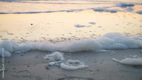 Closeup of red tide algae bloom toxic foam crashing with sunset reflection in Naples beach in Florida Gulf of Mexico on sand photo