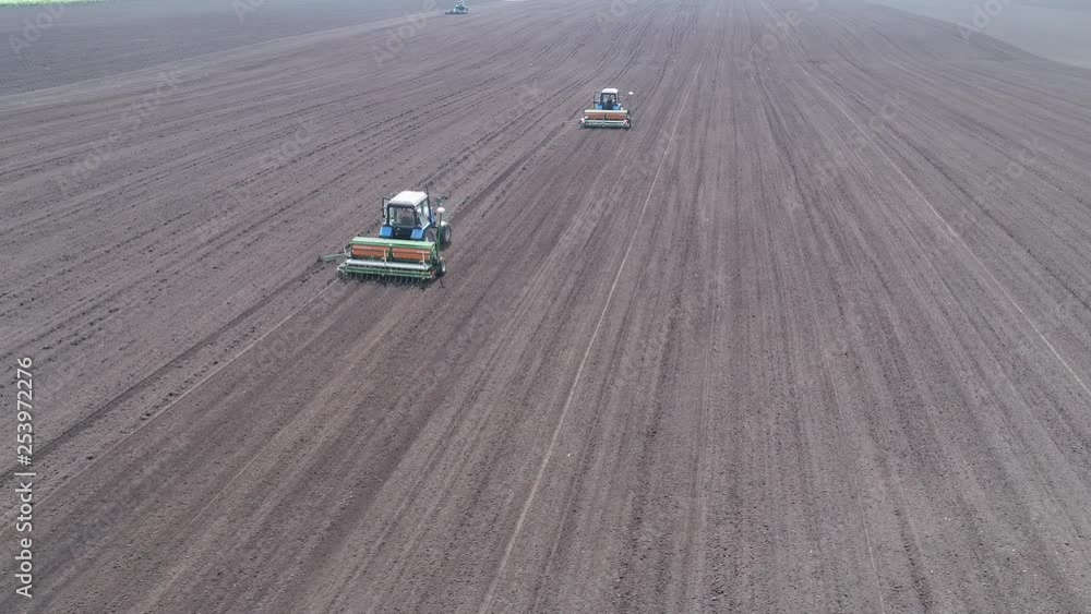 Aerial view of two tractors driving one after another across the field Aerial view of two tractors driving one after another across the field