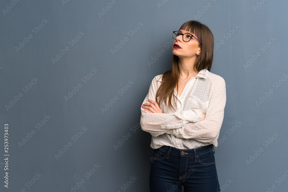 Woman with glasses over blue wall looking up with serious face Woman with glasses over blue wall looking up with serious face