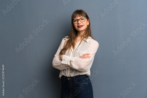 Woman with glasses over blue wall with arms crossed and looking forward