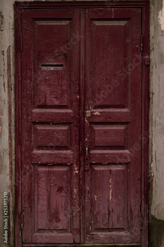 Old wooden door. Grunge wooden door painted maroon. Vintage house facade with a door. Wood vinous texture of a door. Old burgundy grunge texture. Vintage red wooden door.