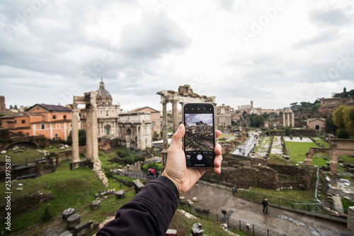 Rome, Italy - November, 2018: Man hands take phone on phone of The Roman Forum beautiful representative picture of antique ruins. The historical center of the Forever City.