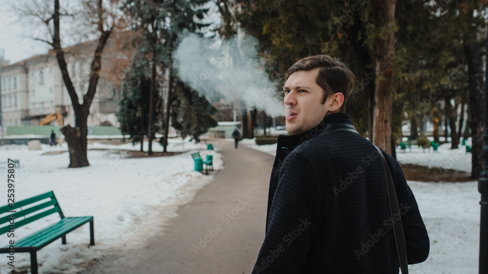 lateral view of a young man in a classic coat smoking outdoors in a park lateral view of a young man in a classic coat smoking outdoors in a park