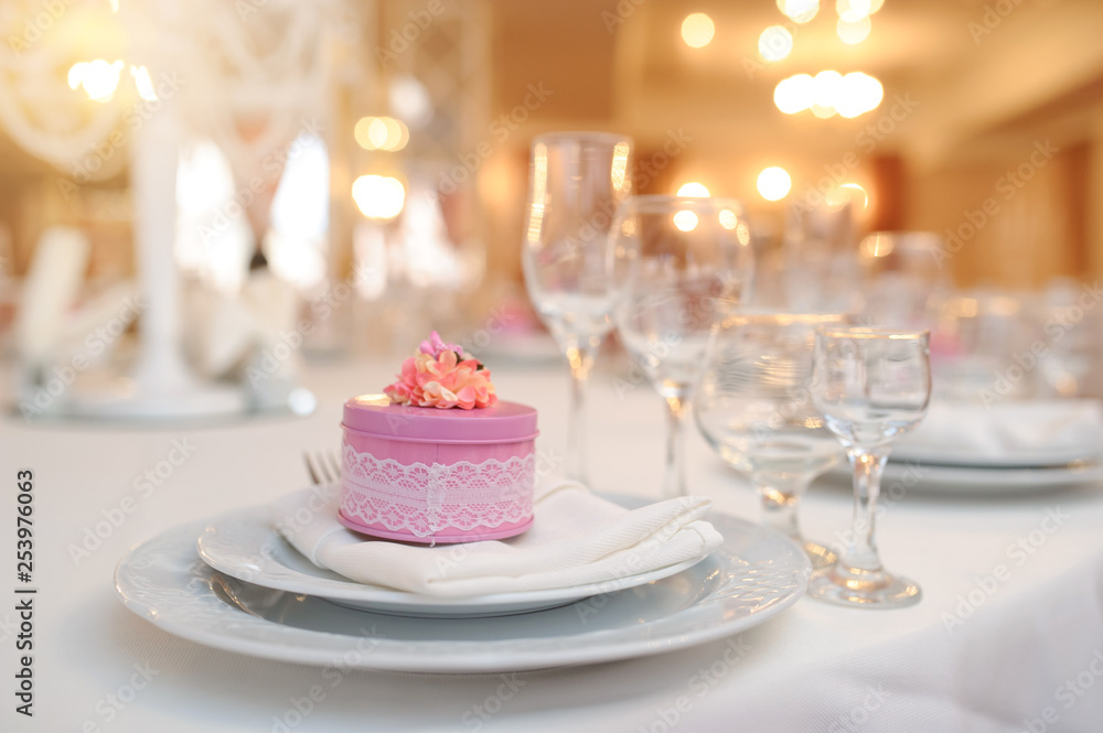 close up photo of knife and fork in a folded napkin on two plate near a set of glasses and a pink round gift box with a flower on the top on the napkin close up photo of knife and fork in a folded napkin on two plate near a set of glasses and a pink round gift box with a flower on the top on the napkin