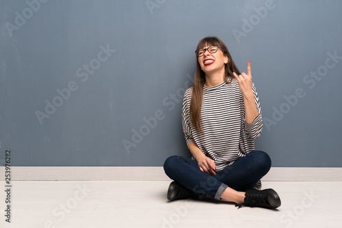 Woman with glasses sitting on the floor making rock gesture