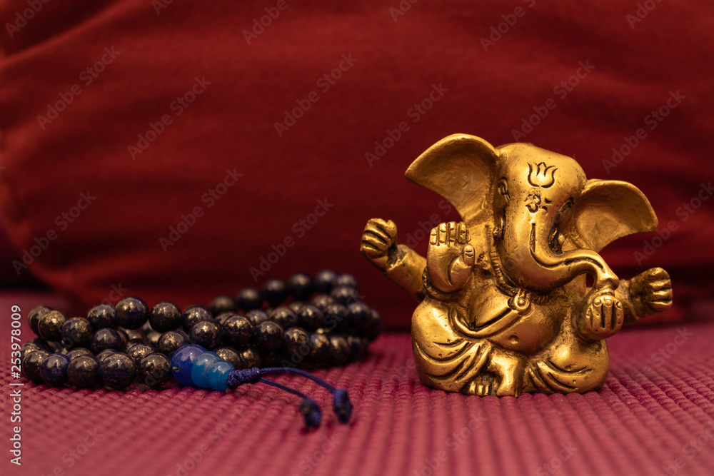 Golden statue of Ganesha with blue mala beads on yoga mat in front of a  yoga pillow. Close up of Japa Meditation accessories. Stock Photo | Adobe  Stock