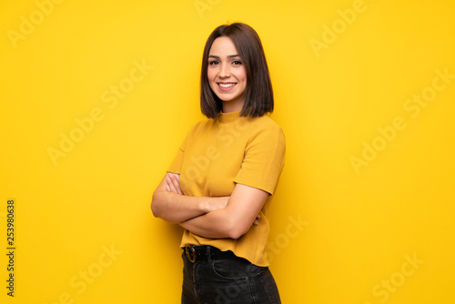 Young woman over yellow wall with arms crossed and looking forward photo