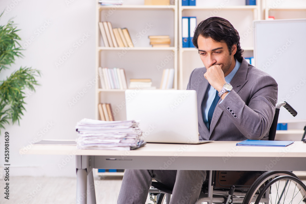 Young handsome employee in wheelchair at the office Young handsome employee in wheelchair at the office