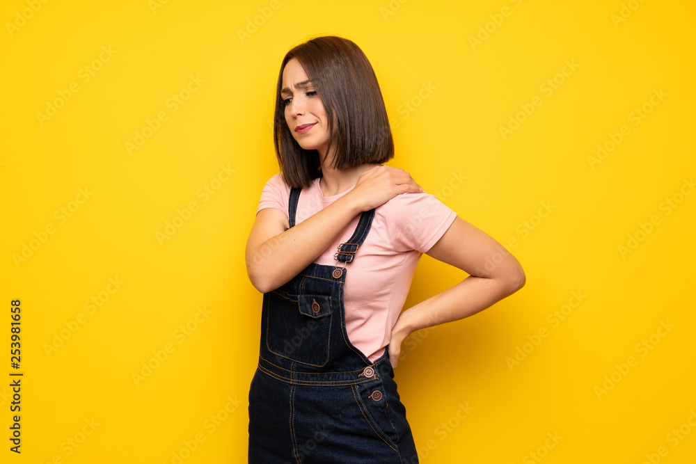 Young woman over yellow wall suffering from pain in shoulder for having made an effort Young woman over yellow wall suffering from pain in shoulder for having made an effort