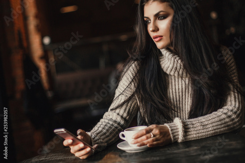 Woman using phone and drinking coffee in a cafe.