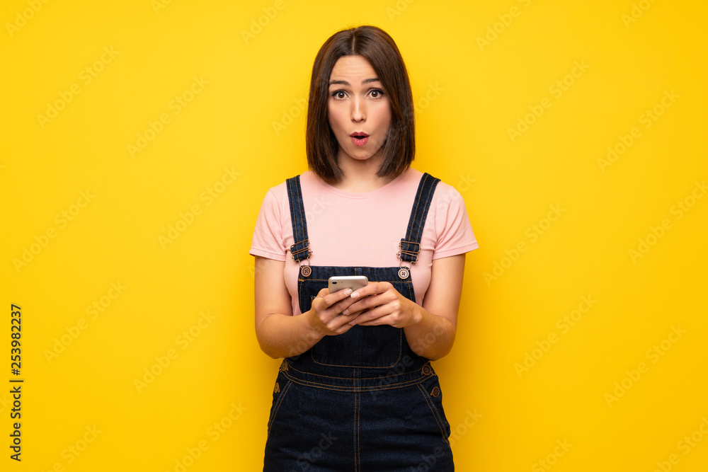 Young woman over yellow wall surprised and sending a message Young woman over yellow wall surprised and sending a message