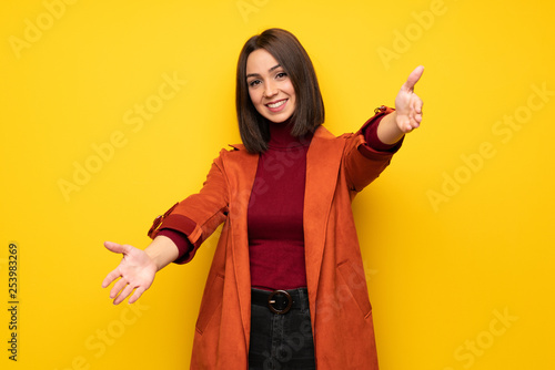 Young woman with coat presenting and inviting to come with hand