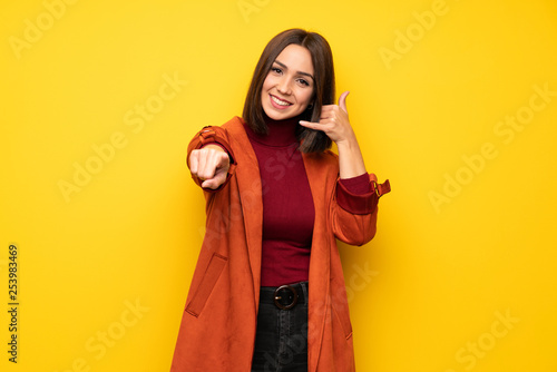 Young woman with coat making phone gesture and pointing front © luismolinero