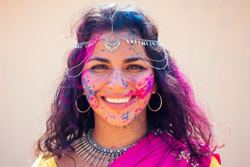 Portrait of young Indian face in paint Woman in traditional indian pink outfit with jeweler celebrating Holi color festival.girl with black hair with bindi on the head and snow-white smile