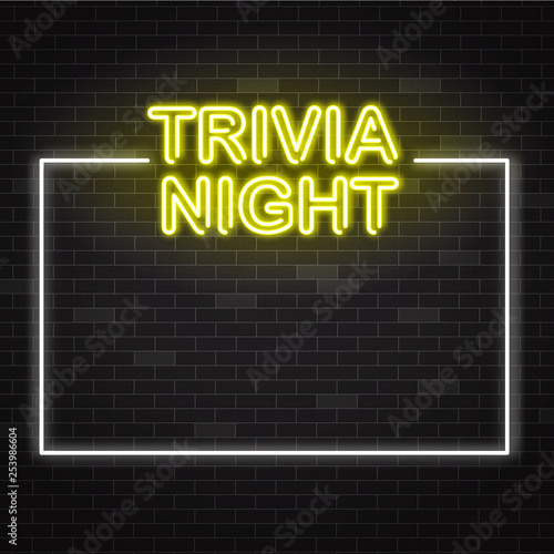 Trivia night yellow neon sign in white frame on dark brick wall background with copy space.