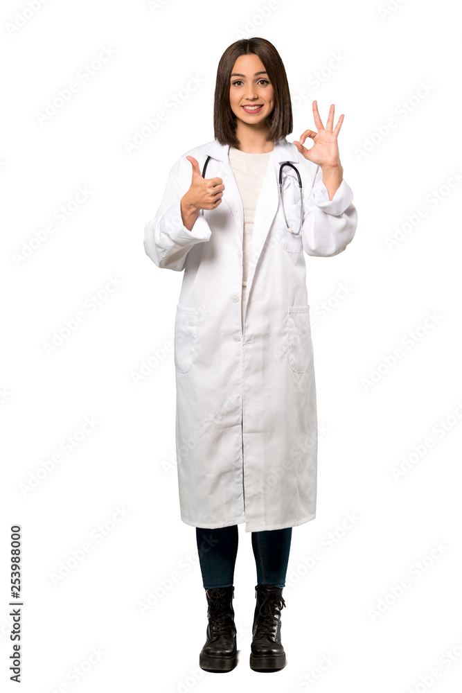 A full-length shot of a Young doctor woman showing ok sign with and giving a thumb up gesture over isolated white background A full-length shot of a Young doctor woman showing ok sign with and giving a thumb up gesture over isolated white background