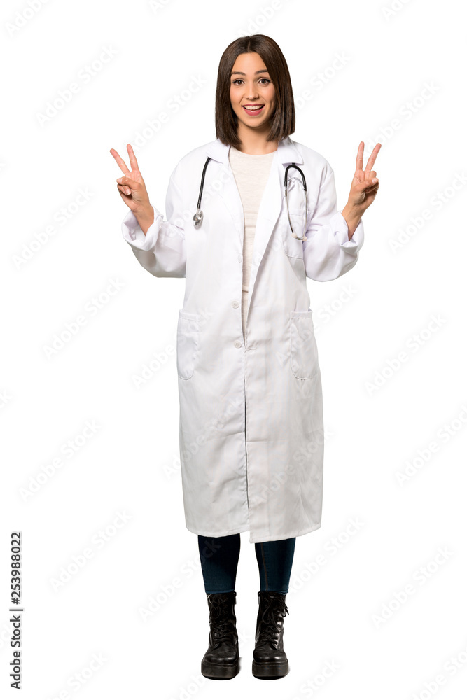 A full-length shot of a Young doctor woman smiling and showing victory sign with both hands over isolated white background A full-length shot of a Young doctor woman smiling and showing victory sign with both hands over isolated white background