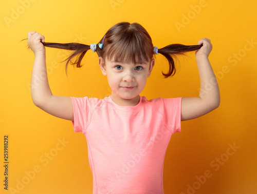 Four-year-old girl in a pink t-shirt on an orange background.