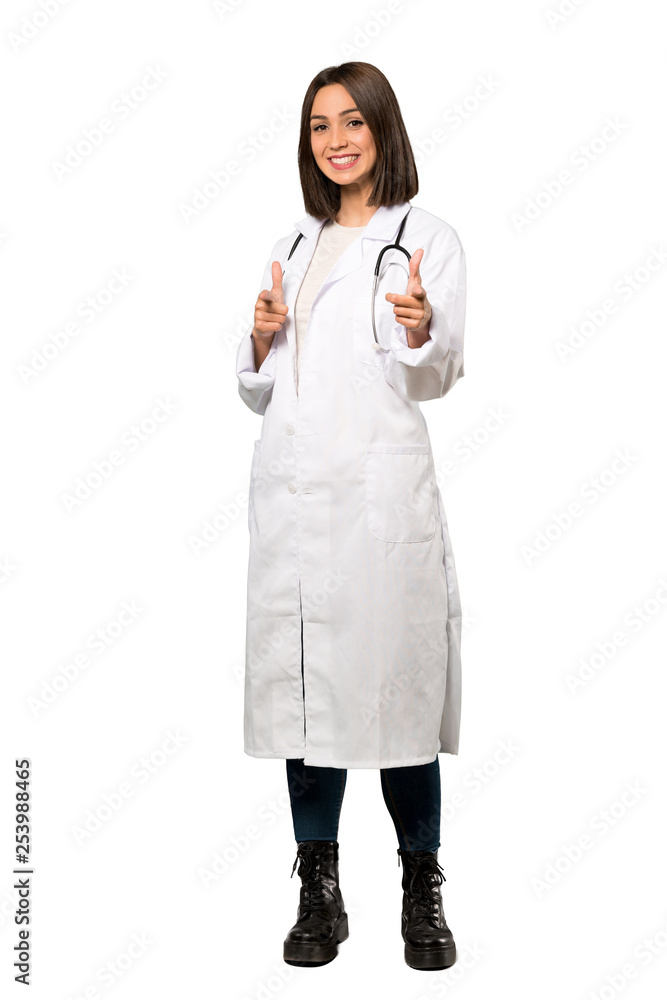 A full-length shot of a Young doctor woman points finger at you while smiling over isolated white background A full-length shot of a Young doctor woman points finger at you while smiling over isolated white background