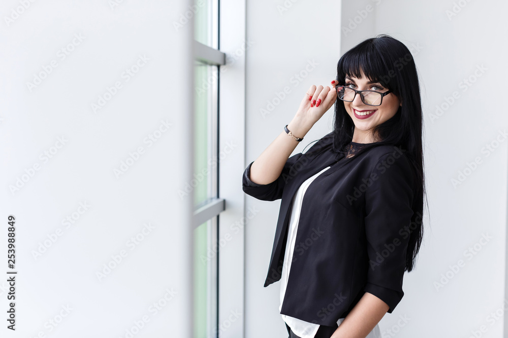 Portrait of young beautiful woman with glasses standing near the window, looking at camera smiling. Portrait of young beautiful woman with glasses standing near the window, looking at camera smiling.