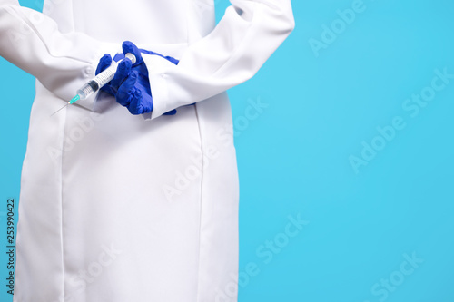 Close up photo of young doctor hands in gloves holding syringe over blue background.