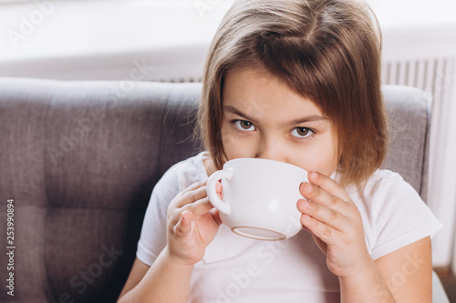 Cheerful cute adorable girl drinking milk in a cup at home