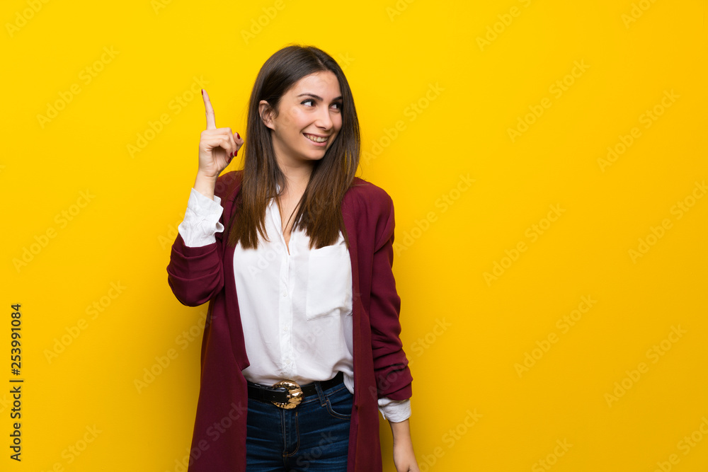Young woman over yellow wall intending to realizes the solution while lifting a finger up Young woman over yellow wall intending to realizes the solution while lifting a finger up