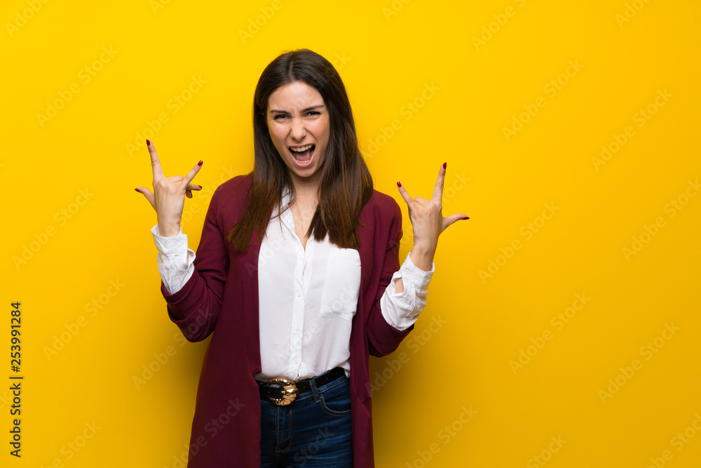 Young woman over yellow wall making rock gesture Young woman over yellow wall making rock gesture