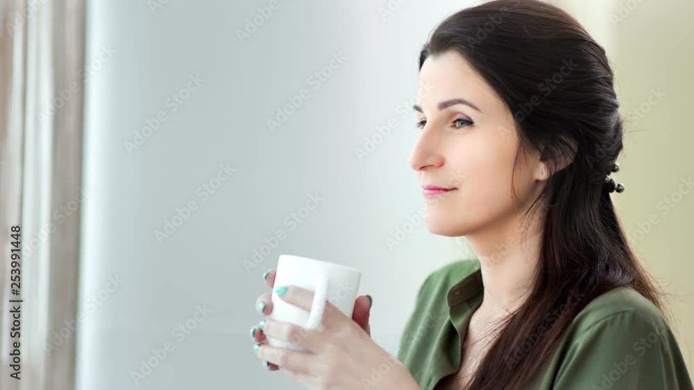 Medium close-up pensive smiling woman dreaming drinking hot beverage from white big mug Medium close-up pensive smiling woman dreaming drinking hot beverage from white big mug