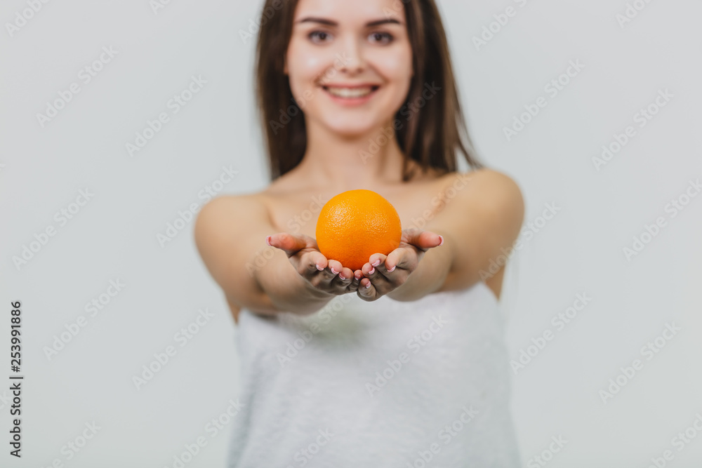 Portrait of a cute young attractive half-eyed woman holding an orange orange on her hands and looking at the camera, isolated over a white background. Orange on the blurred background of the girl. Portrait of a cute young attractive half-eyed woman holding an orange orange on her hands and looking at the camera, isolated over a white background. Orange on the blurred background of the girl.