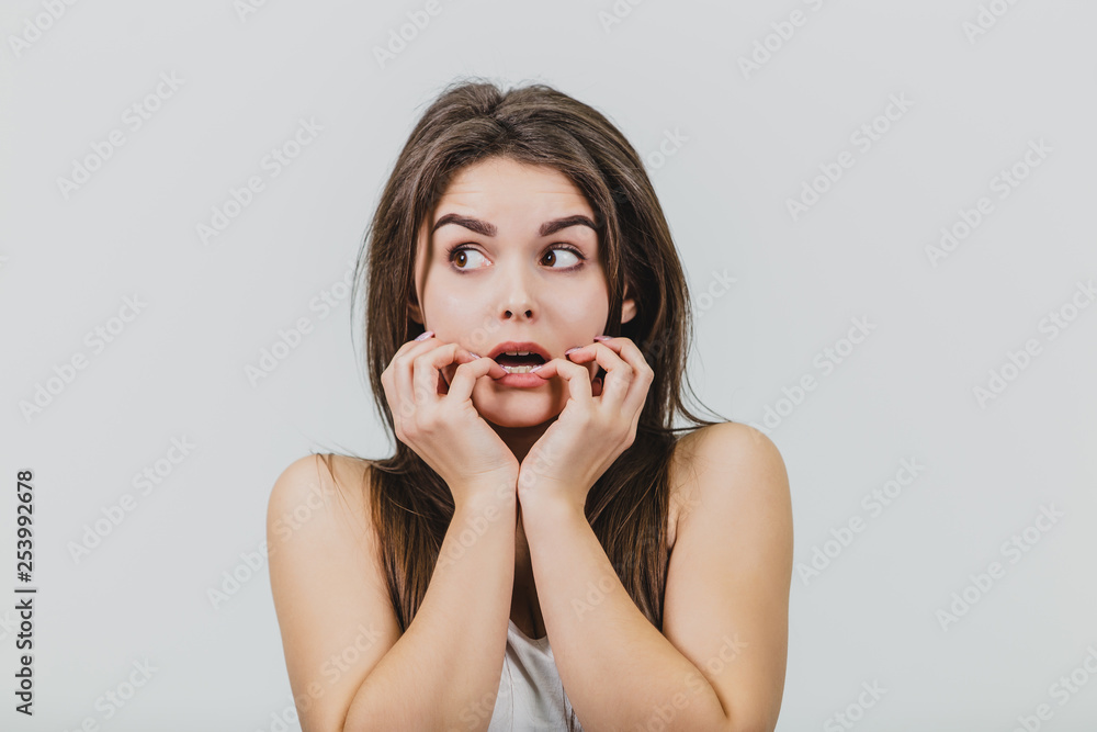 Young girl is pretty Caucasian standing in a white background. For this time dressed in a white T-shirt and blue jeans. During this time, she put his hands on his face with astonishment. Has beautiful