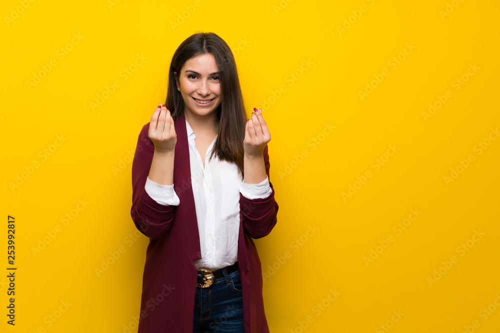Young woman over yellow wall making money gesture Young woman over yellow wall making money gesture