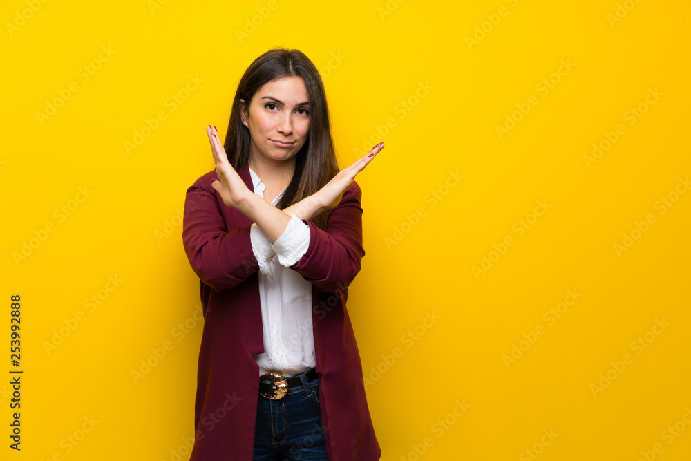 Young woman over yellow wall making NO gesture Young woman over yellow wall making NO gesture