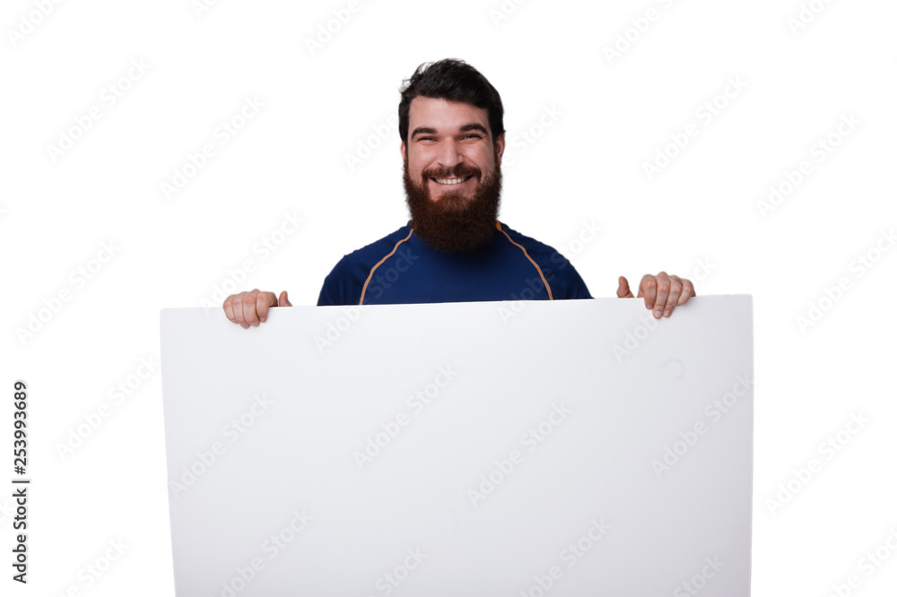 Front view. Portrait of smiling bearded guy holding blank white banner in his hands. Mock up, copy space for your text. Front view. Portrait of smiling bearded guy holding blank white banner in his hands. Mock up, copy space for your text.