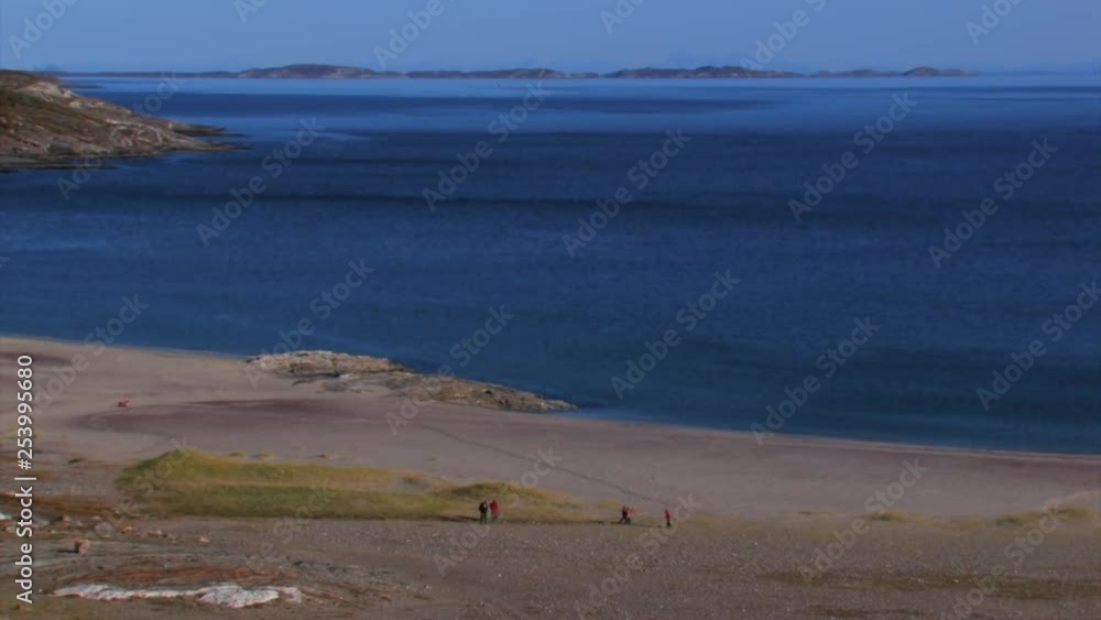 People play on a wide empty beach near beautiful blue water. A family enjoying the day at the beach. View from high on a hillside. People play on a wide empty beach near beautiful blue water. A family enjoying the day at the beach. View from high on a hillside.