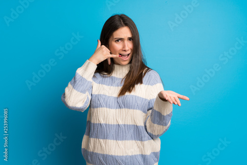 Young woman over blue wall making phone gesture and doubting