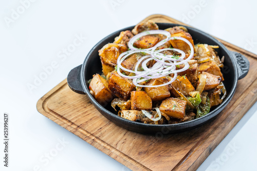 Fried potatoes with meat, broccoli and red onions decorated with rosemary in a frying pan on a wooden table top view