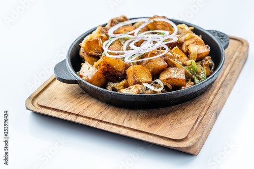 Fried potatoes with meat, broccoli and red onions decorated with rosemary in a frying pan on a wooden table top view