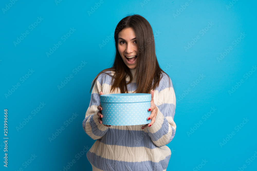 Young woman over blue wall surprised because has been given a gift Young woman over blue wall surprised because has been given a gift