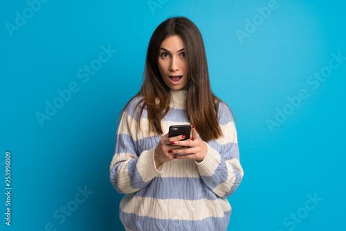 Young woman over blue wall surprised and sending a message