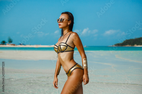 Fashion outdoor photo gorgeous sexy woman in a luxurious gold bikini, perfect dark tanned skin. Tropical island trip