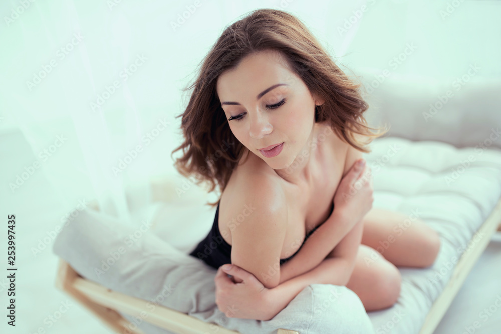 Beautiful brunette girl in short black dress is lying on sofa and posing sensual with delicate skin on her bare shoulders. Beautiful brunette girl in short black dress is lying on sofa and posing sensual with delicate skin on her bare shoulders.
