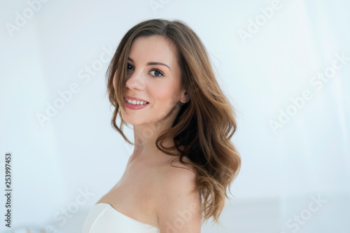 Expression photo of smiling brunette in white dress, on white background. Concept of delicacy, chastity and innocence of woman.